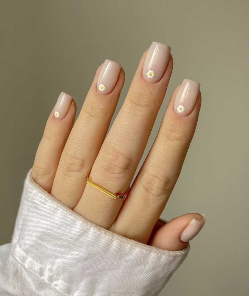 Close-up of nails with a nude base and tiny white daisy accents.